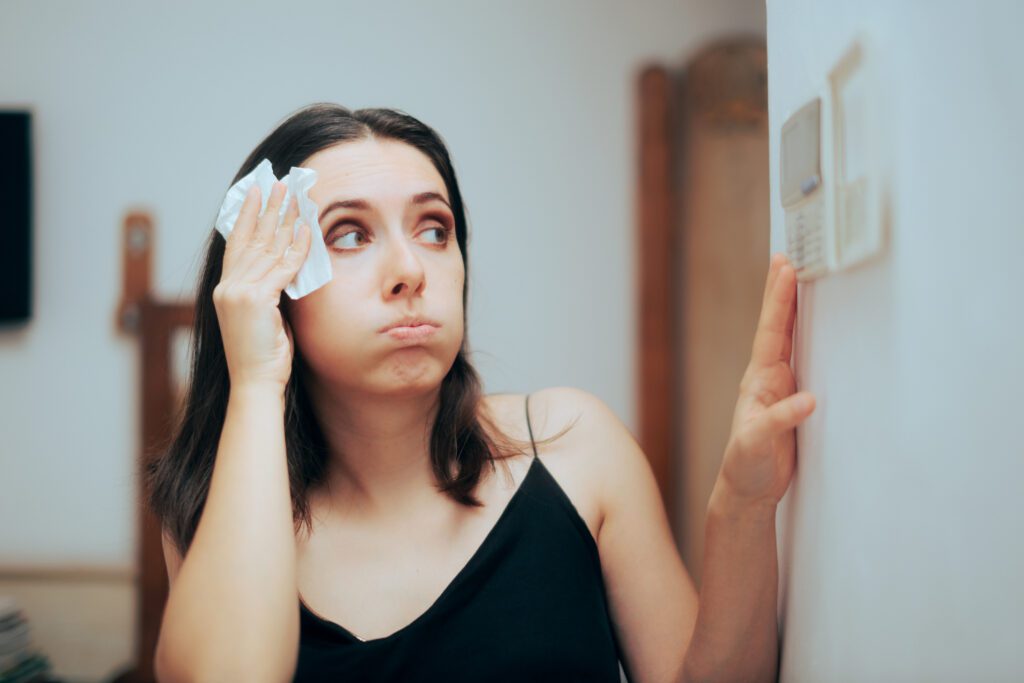 woman looking at her thermostat and suffering in the heat because of a broken a/c